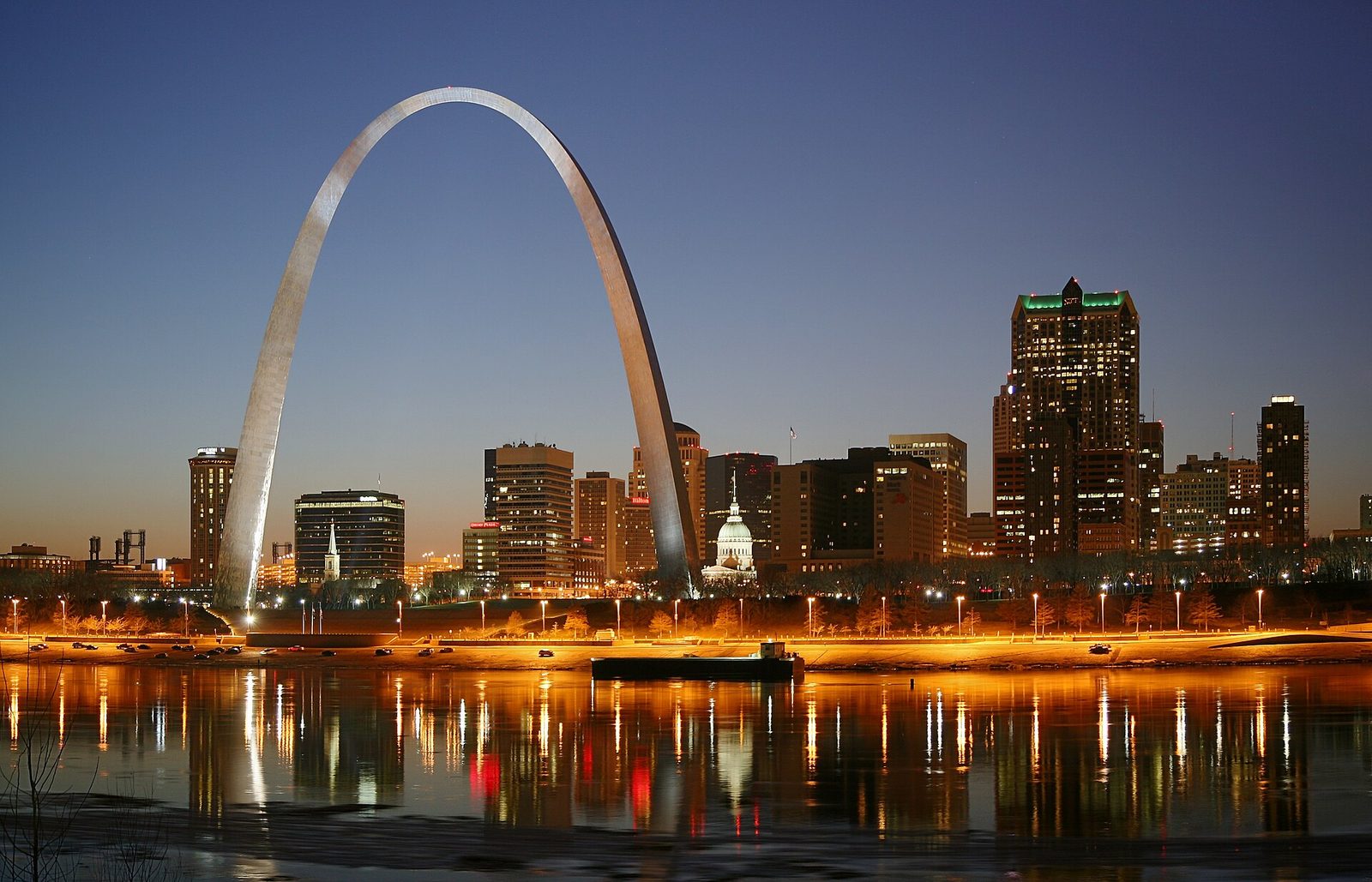 The Gateway Arch and the downtown St. Louis skyline at night, lights reflected in the river