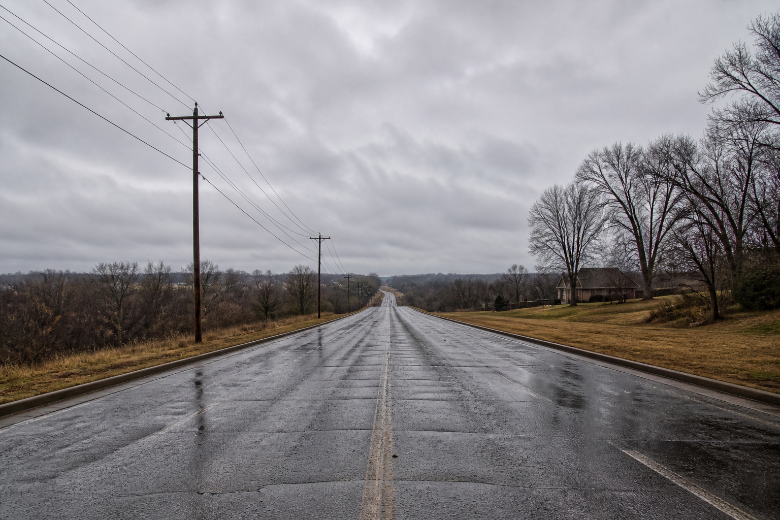 A wet empty suburban Missouri road after rain under an overcast sky.